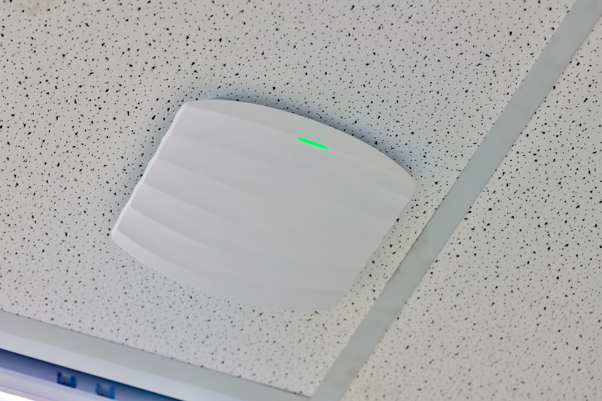 Access point Wi-Fi con spia verde accesa, installato su un controsoffitto a quadrotti