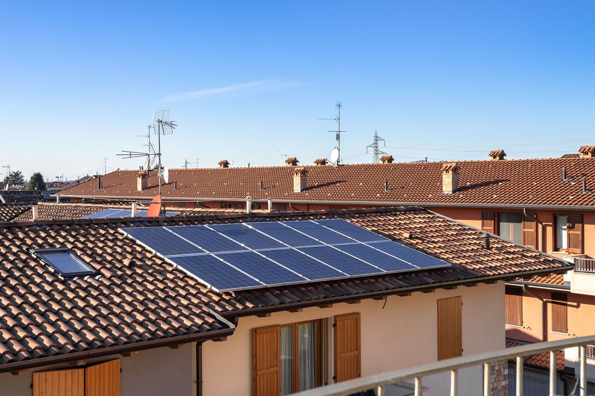 Pannelli fotovoltaici sulla falda in coppi di una casa a schiera, sotto un cielo sereno