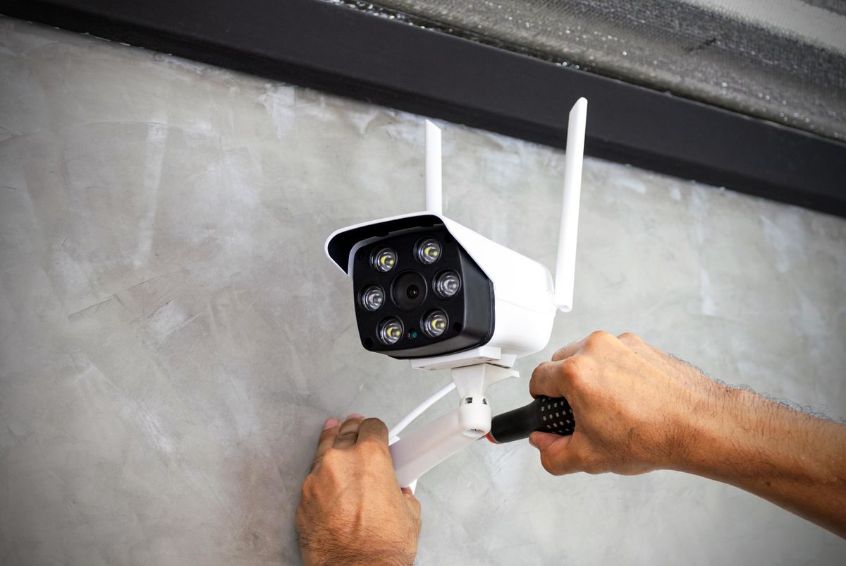 Tecnico che installa con un cacciavite una telecamera IP bullet a infrarossi su una parete esterna