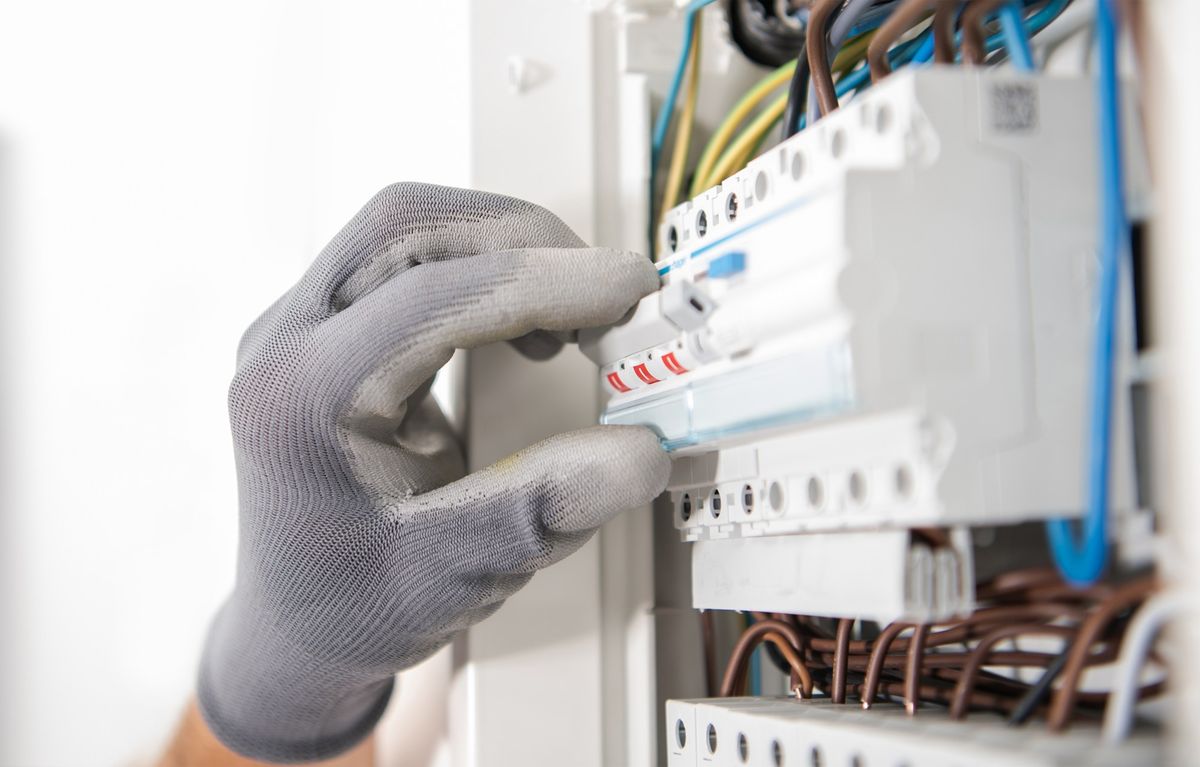 Mano con guanto da lavoro che aziona un interruttore in un quadro elettrico