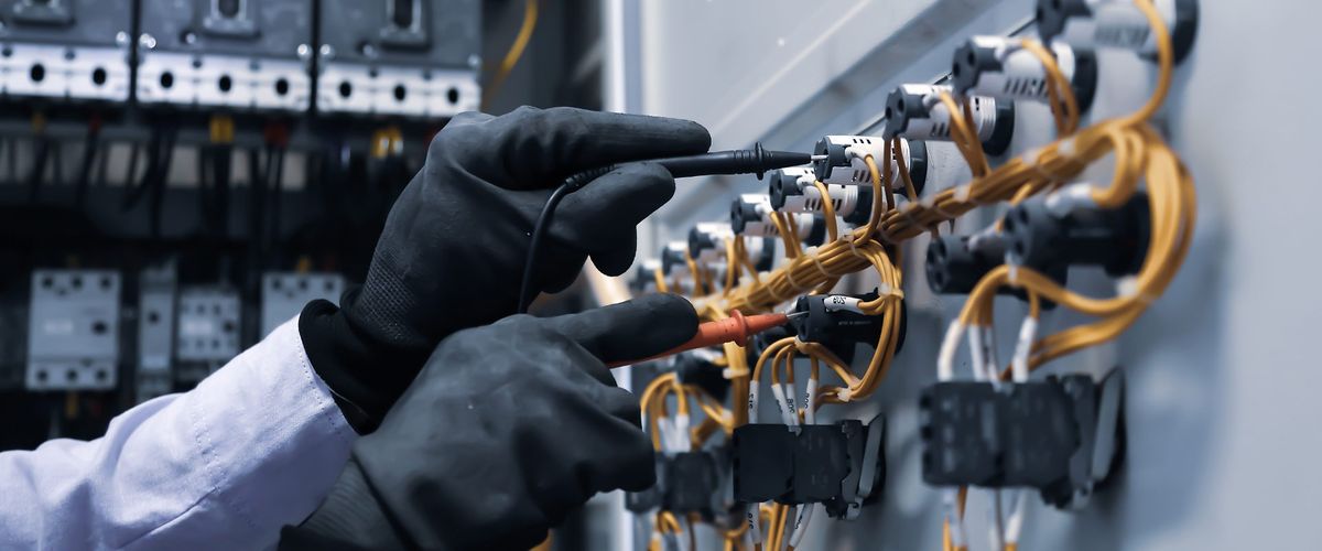 Mani con guanti isolanti che eseguono misure con i puntali su un quadro elettrico